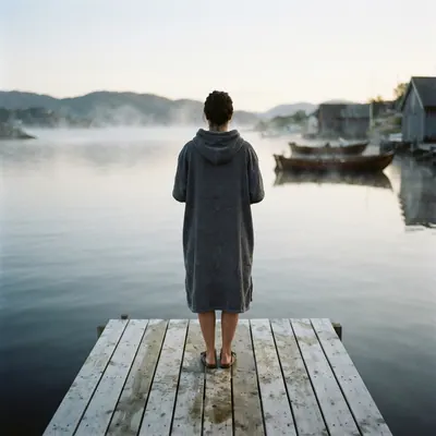 A person in a hooded poncho on a jetty, seen from behind